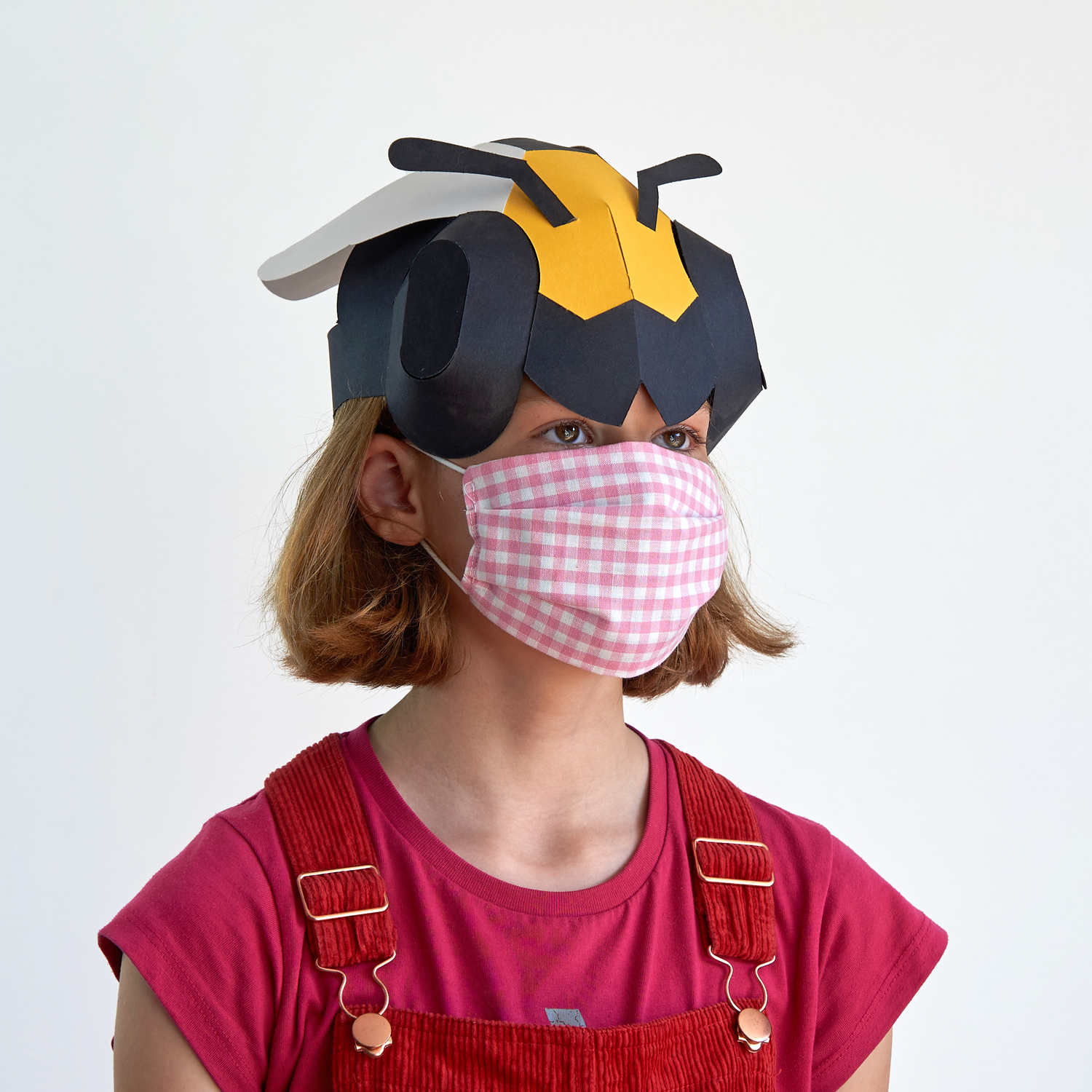 Person wearing a paper bee hat and red overalls on a white background