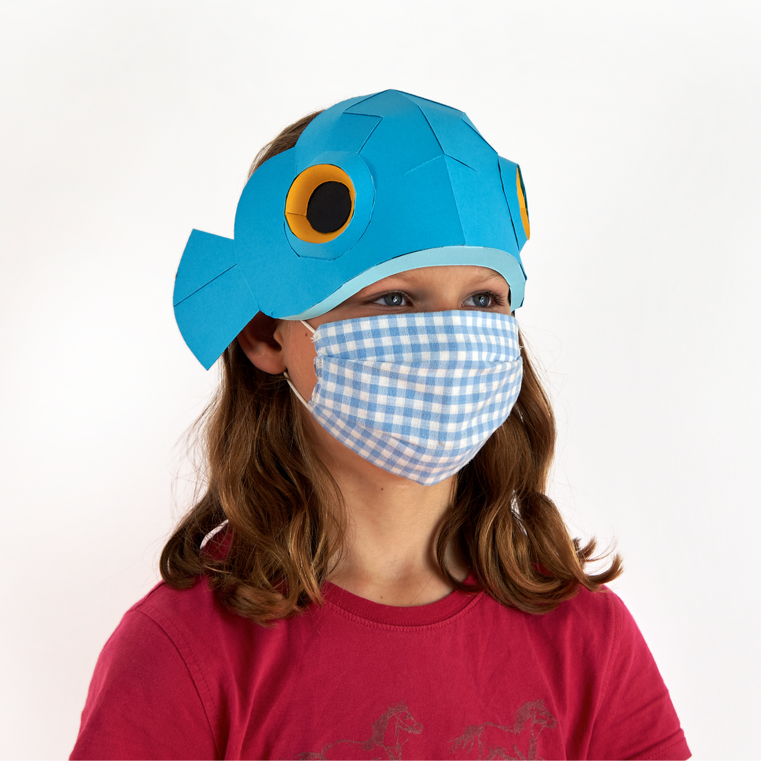 Child wearing a blue fish-shaped hat and checkered mask on a white background